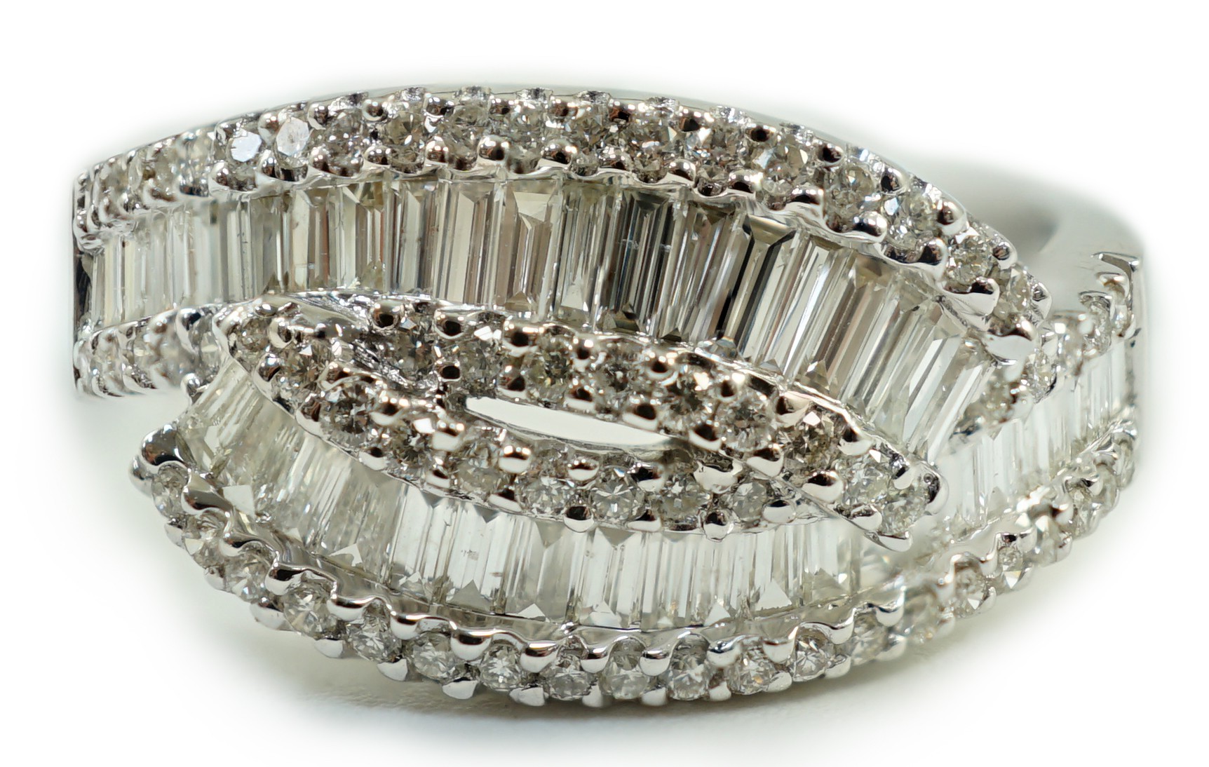 A modern 18ct white gold, baguette cut and diamond chip cluster set crossover ring, size O, gross weight 4.7 grams.